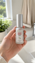 Hand holding Nano Soma Liquid bottle near a bright window with greenery